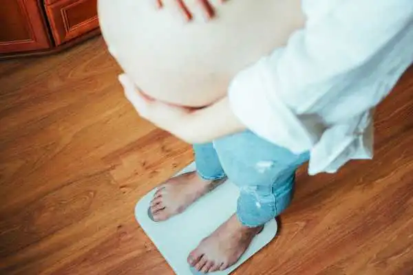 Image of woman weighing herself and experiencing weight gain through pregnancy Stowmarket